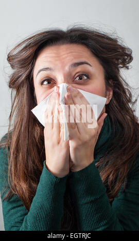 Young woman blowing her nose with paper tissue on gray background. Stock Photo