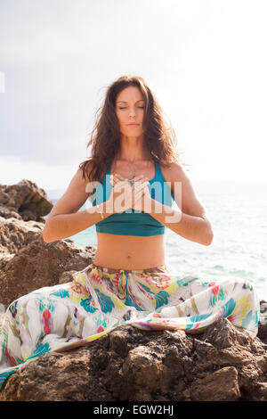 Woman meditating on rocks near ocean. Stock Photo