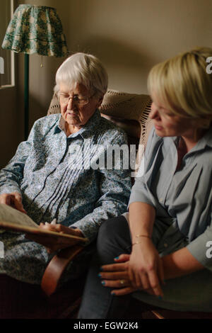 Senior woman in blue shirt sitting in chair, with younger woman next to her. Stock Photo