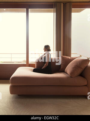Woman kneeling on sofa, looking out the window.