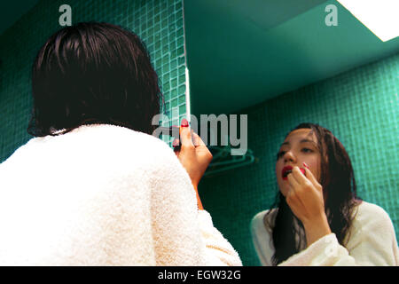 Woman putting on lipstick in mirror. Stock Photo