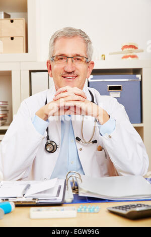 Smiling old physician sitting at his desk in the office Stock Photo