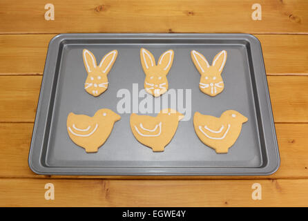 Iced Easter biscuits in bunny and chick shapes on a baking tray on a kitchen table Stock Photo
