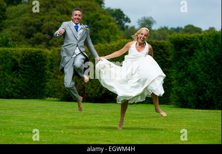 A recently married couple run around jumping in excitement of just completing their vows and becoming husband and wife. Stock Photo