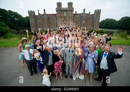 A group shot of a wedding at Herstmonceux castle in East Sussex, UK. Everyone cheers in celebration for the happy couple. Stock Photo
