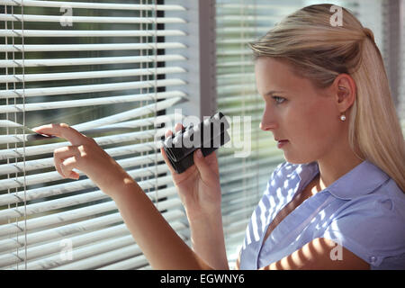 Nosy woman peering through some blinds Stock Photo