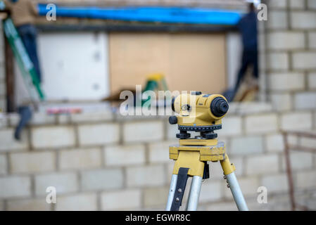 Grey gray besser cinder block breezeblock CMU concrete masonry unit wall defocused behind a yellow theodolite. Stock Photo