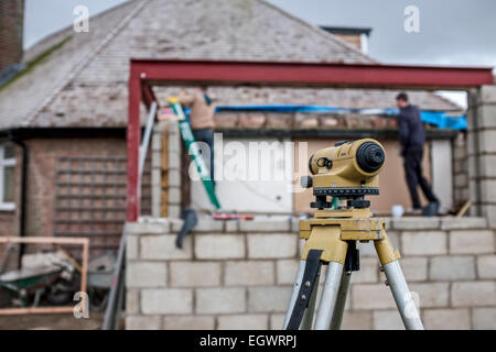 Theodolite on a residential construction site, building a house extension. Two labourers are defocused in the background. Stock Photo