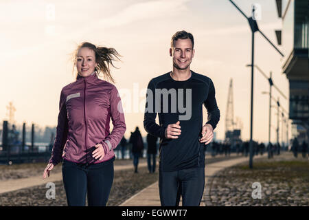 Active young couple jogging side by side in an urban street during their daily workout in a health and fitness concept Stock Photo