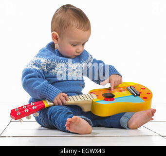 Baby boy (12.5 months) sitting playing with toy guitar Stock Photo