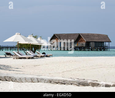 Sun-loungers and parasols on the beach at an island resort in the Maldives with one of the villas in the distance Stock Photo