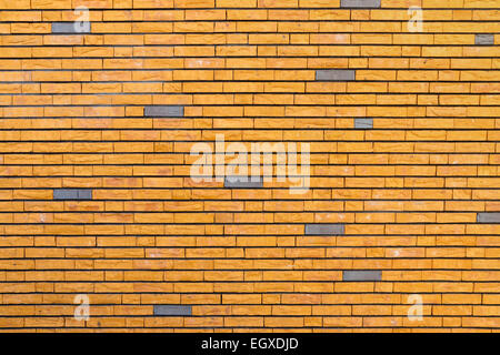 Yellow brick wall with  irregular surface interspersed with some gray bricks Stock Photo