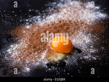 Dusted wheat flour, cocoa powder and egg on dark background, selective focus Stock Photo