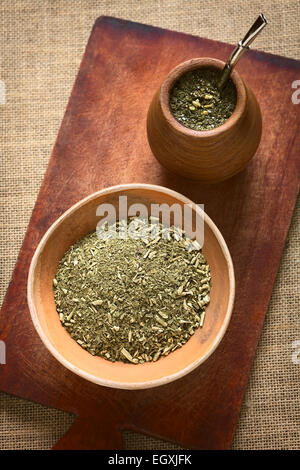 South American yerba mate (mate tea) dried leaves in clay bowl with a wooden mate cup filled with tea Stock Photo