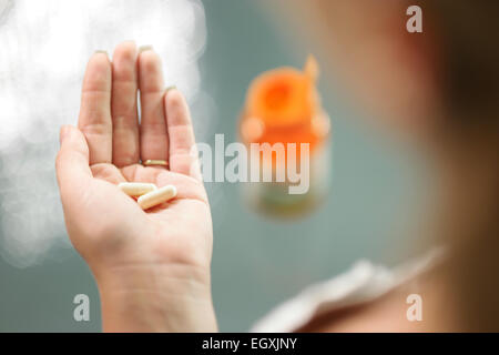 Close up view of young woman holding ginseng vitamins and minerals pills in hand with capsule bottle on table. High angle view Stock Photo