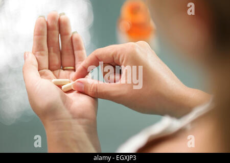 Close up view of young woman holding ginseng vitamins and minerals pills in hand with capsule bottle on table. High angle view Stock Photo