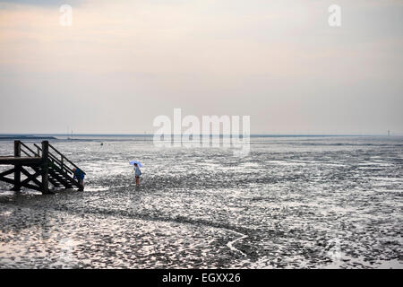 Young woman walking in the mudflats of the Wadden Sea (Wattenmeer) at low tide Stock Photo
