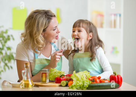 Mother feeding child vegetables. Mom feeds kid in white kitchen with ...