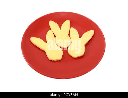 Three rabbit-shaped cookies for Easter on a red plate, isolated on a white background Stock Photo