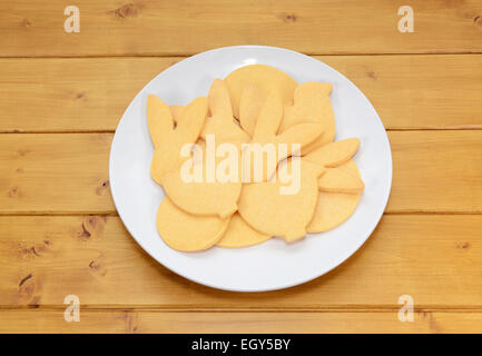 Pile of cookies in Easter-themed shapes on a white plate on a wooden table Stock Photo