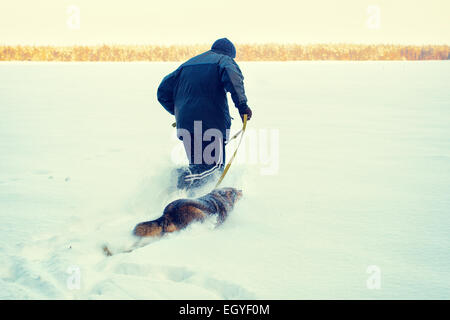 Man running with dog on the snowy field back to camera Stock Photo