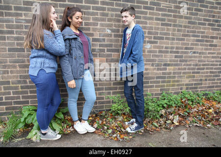 Teenage girls talking to teenage boy  leaning on wall - model released Stock Photo