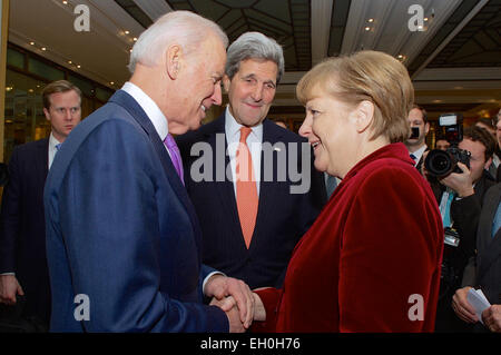 U.S. Secretary of State John Kerry watches as Vice President Joe Biden greets German Chancellor Angela Merkel after she arrived at the Munich Security Conference in Munich, Germany, on February 7, 2015, to deliver a speech and meet with U.S., Ukrainian, and other government officials. Stock Photo