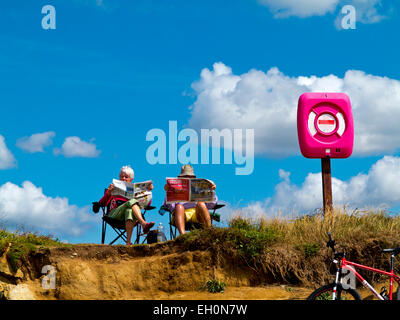 Elderly couple sitting on deck chairs reading on the beach at Burton Bradstock in Dorset on the south west coast of  England UK Stock Photo