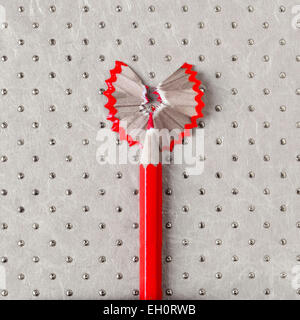 a sharpened wooden red coloured pencil with its shavings forming a heart on a patterned background Stock Photo