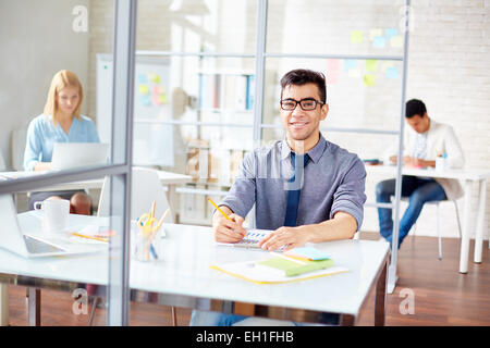 Happy young businessman working in office on background of his colleagues Stock Photo