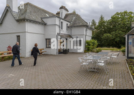 Two senior adults  a couple walk toward Queens' View Visitor Centre Center, Tay Forest Scotland. Cafeteria tables and chairs. Stock Photo