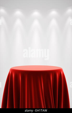 Round presentation pedestal covered with a red silk cloth in front of a white wall illuminated by a spot light Stock Photo