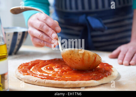 Close Up Of Adding Tomato Sauce To Pizza Base Stock Photo