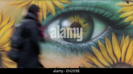 A pedestrian walks past a graffio which shows an eye peaking through flowers, painted on the wall of a house in Gera, Germany, 11 February 2015. Photo: Sebastian Kahnert/dpa Stock Photo