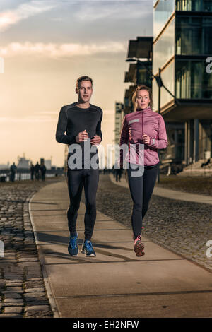 Active young couple jogging side by side on a harbor promenade at sunset during their daily workout in a health and fitness conc Stock Photo