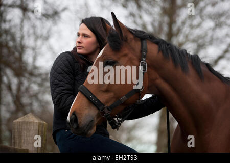 A young woman sitting on a fence, holding a horse Stock Photo