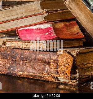 Old, slightly neglected books stacked on top of each other on a wooden bookshelf. Stock Photo