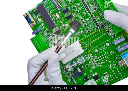 Closeup of white gloved hands using a brush to clean a new green computer electronic circuit board with CPU isolated on white Stock Photo