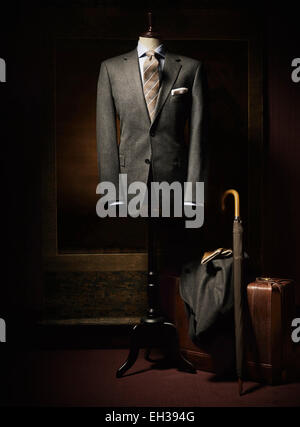 Suit jacket, shirt and tie displayed on dress form with suitcase, coat, gloves and an umbrella beside on floor, studio shot Stock Photo