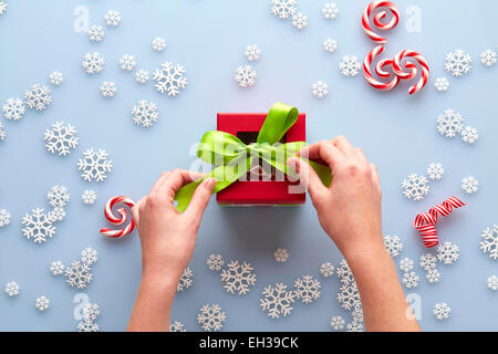 Overhead View of Hands Tying Bow on Present with Snowflakes and Candy Cane Swirls, Studio Shot Stock Photo
