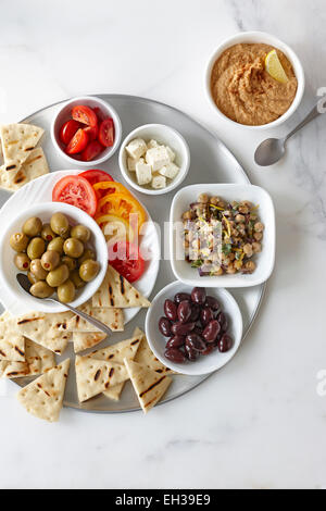 Overhead View of Appetizers, Chickpea Salad, Feta, Cherry and Sliced Tomatoes, Green and Black Olives, Hummus, and Grilled Pita Stock Photo