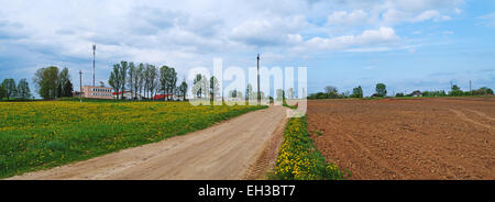 Ploughed spring field. Sand road near the farm. Evening sunlight. Stock Photo