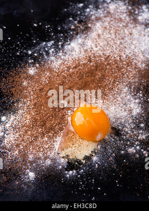 Dusted wheat flour, cocoa powder and egg on dark background, selective focus, top view Stock Photo