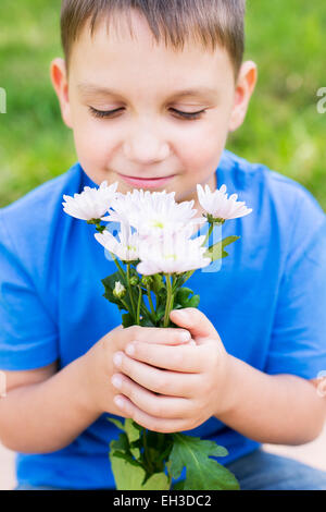 Boy holding flowers and smelling them. Selective focus Stock Photo