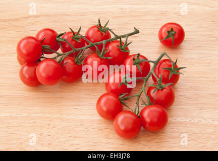 Small piccolo cherry tomatoes on the vine on a pale wood background. Stock Photo