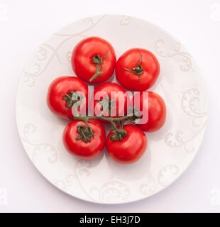 Large beefsteak tomatoes on the vine on a white plate. Stock Photo