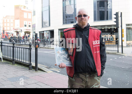 A homeless man stands on the streets of Brighton selling the Big Issue Magazine to make a better life for himself Stock Photo