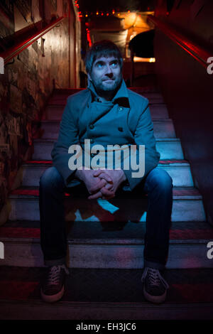 a bar owner sits on some steps in his pub in Brighton lit by blue light Stock Photo