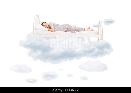 Young man sleeping on a comfortable bed in clouds isolated on white background Stock Photo