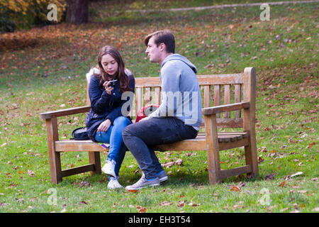 young couple sat on bench with young woman looking at photos on camera Stock Photo